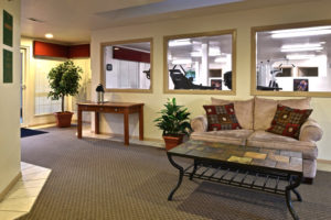 lobby with couch and coffee table, windows looking into fitness center
