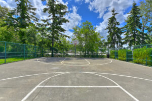Exterior basketball court, fenced in, trees in background, photo taken on a sunny day